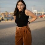 Woman in black crop top and brown pants posing outdoors at sunset.